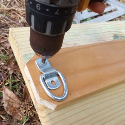 Close up of a drill installing a low profile metal tie ring into wood board.