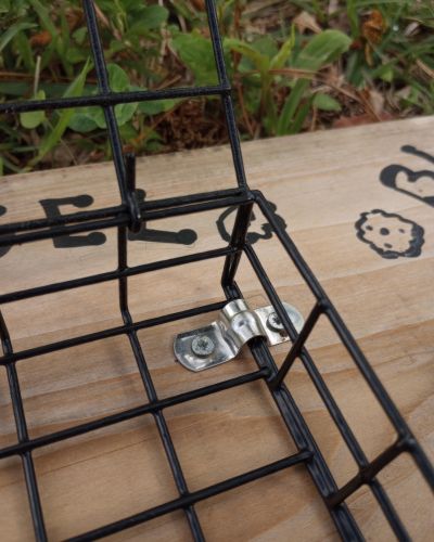 Close up of small cable bracket or tie holding suet cage to wooden board for a DIY horse enrichment project.